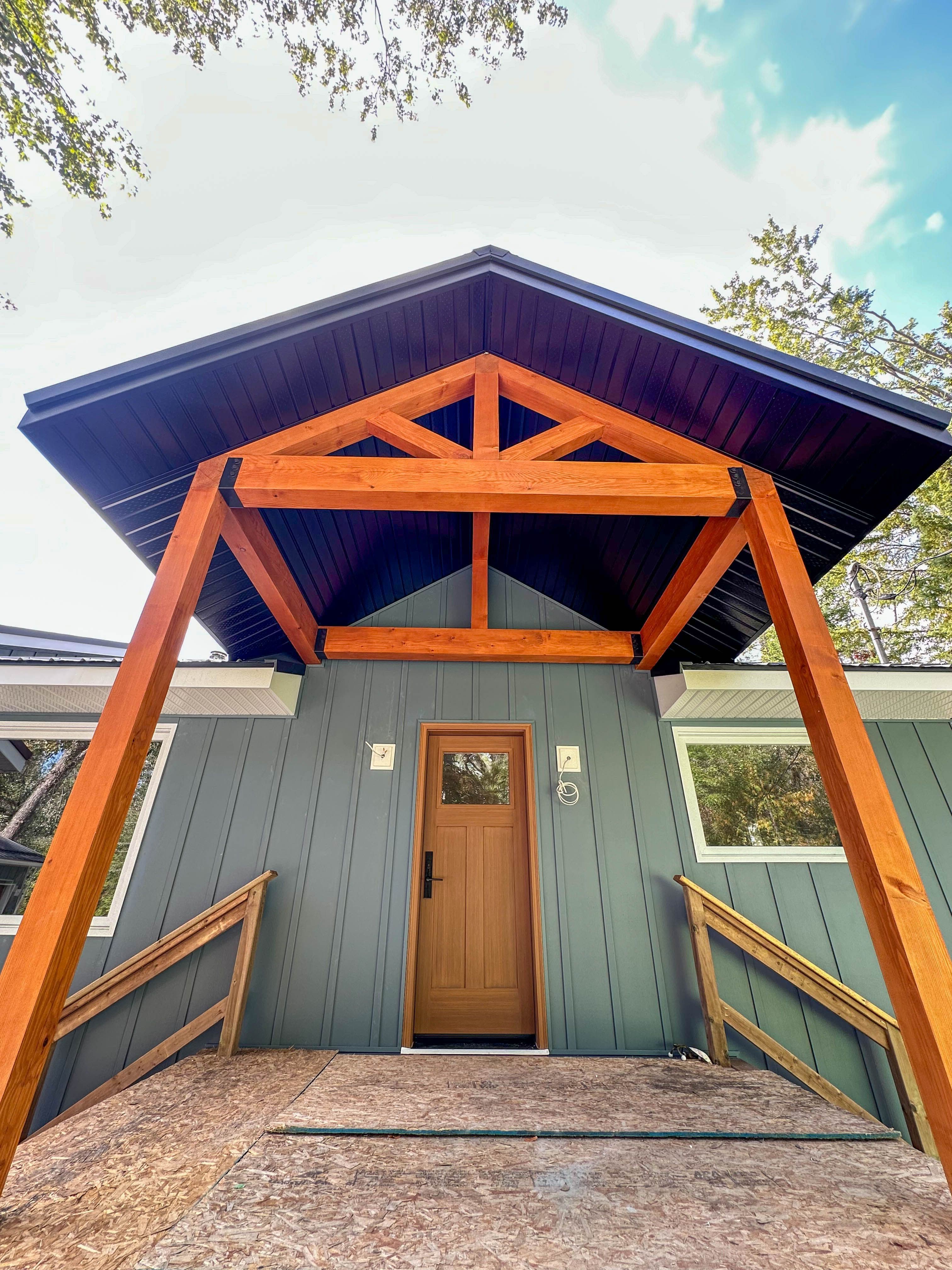Front porch of modern home featuring timber posts, black soffit, and blue board and batten siding