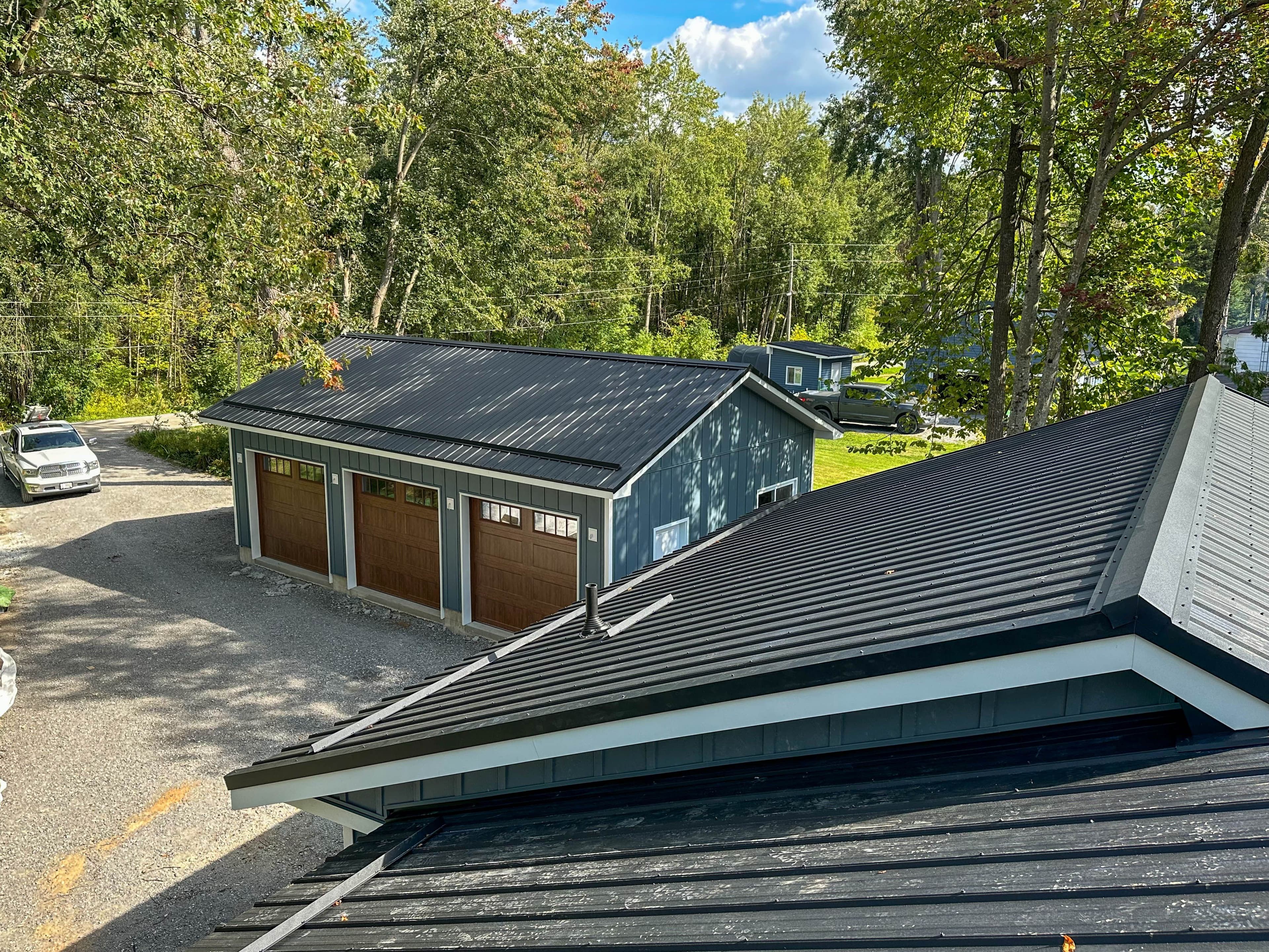 Aerial view of black steel roofs on modern home and garage surrounded by trees in Fenelon Falls