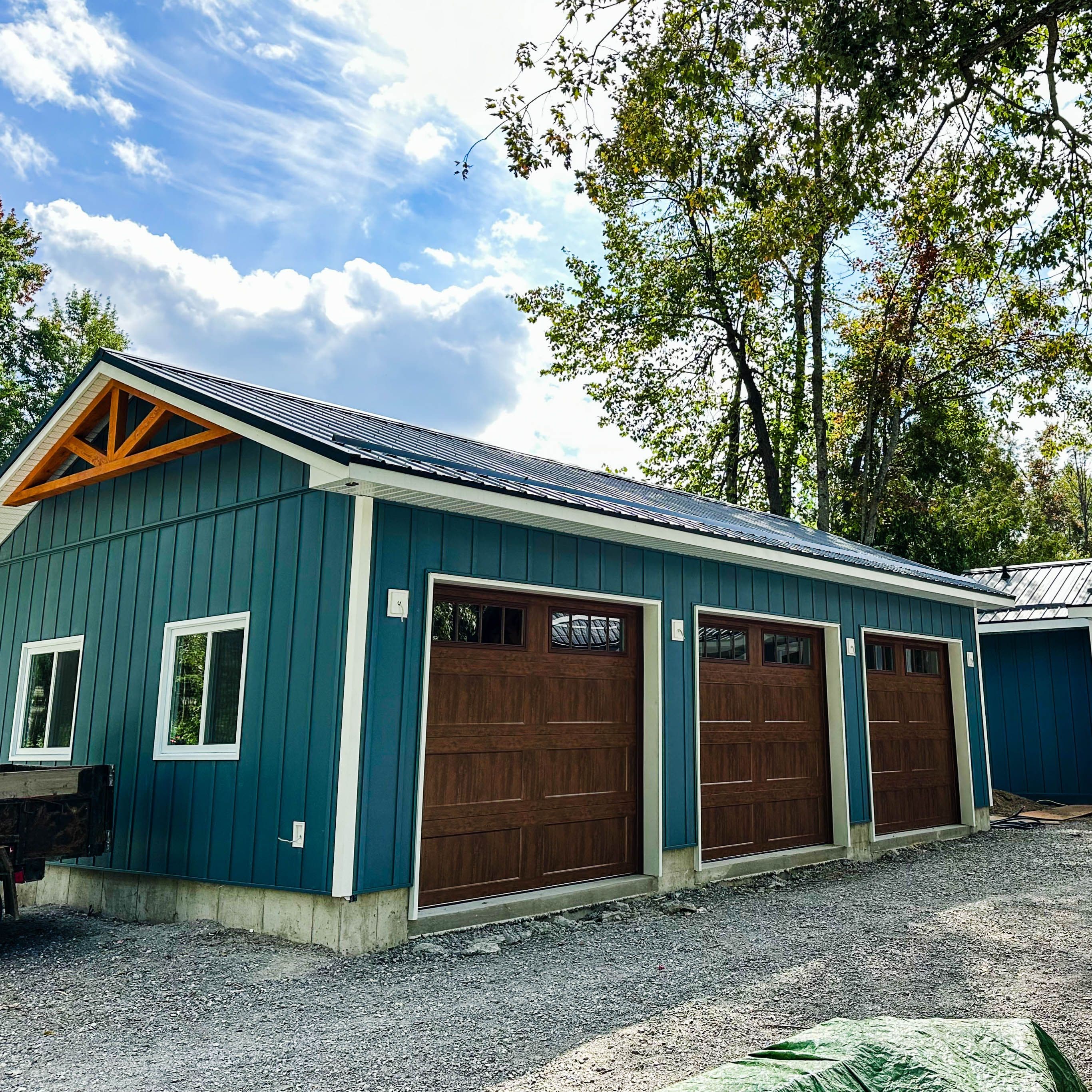 Three-car garage with wood-tone doors, blue composite siding, and steel roof connected to main home