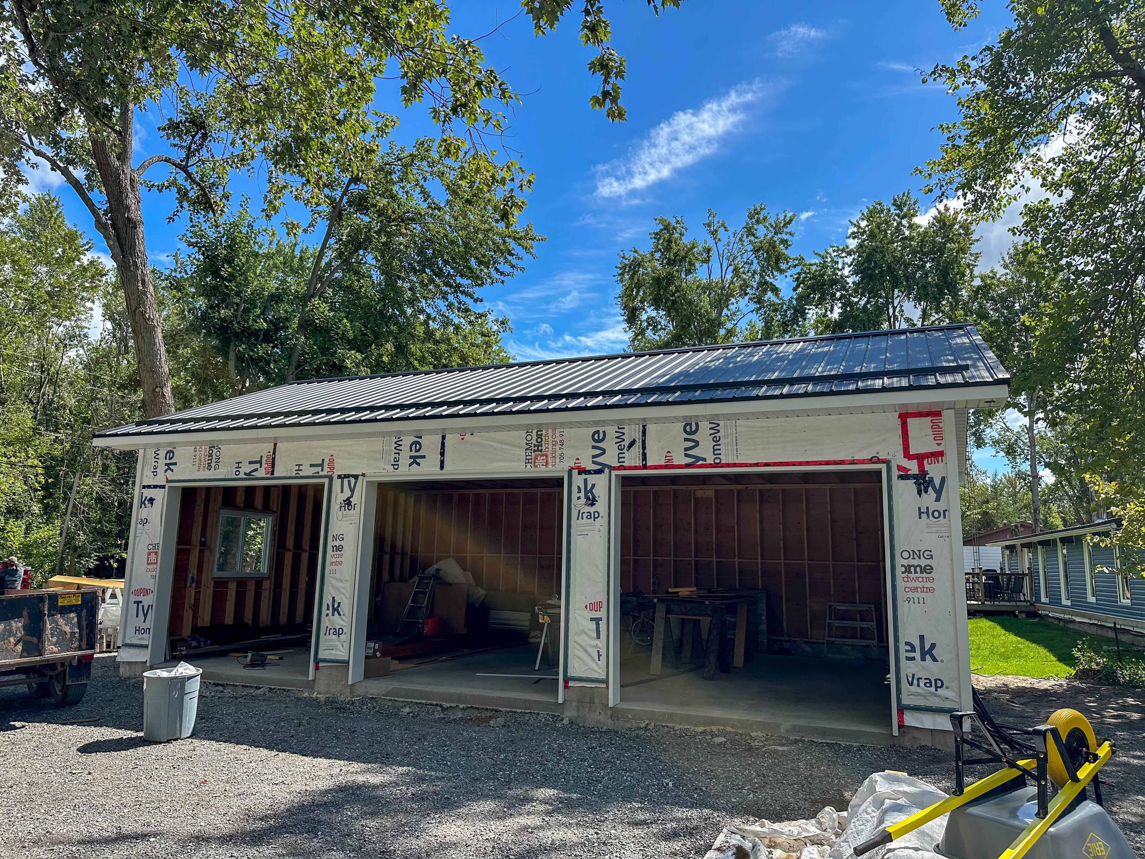 Garage structure with Tyvek wrap and exposed fastener steel roof installation underway