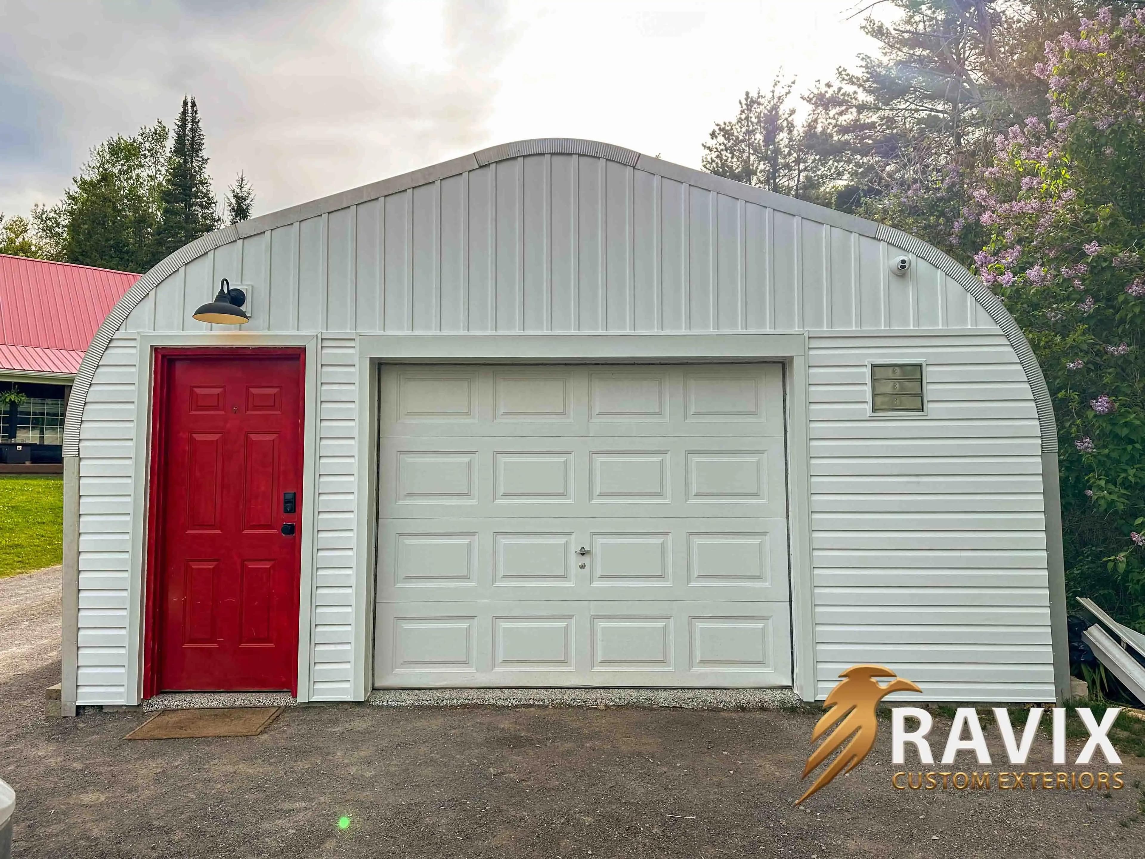 White garage exterior with curved roofline, red entry door, large overhead garage door, and vertical and horizontal siding details.