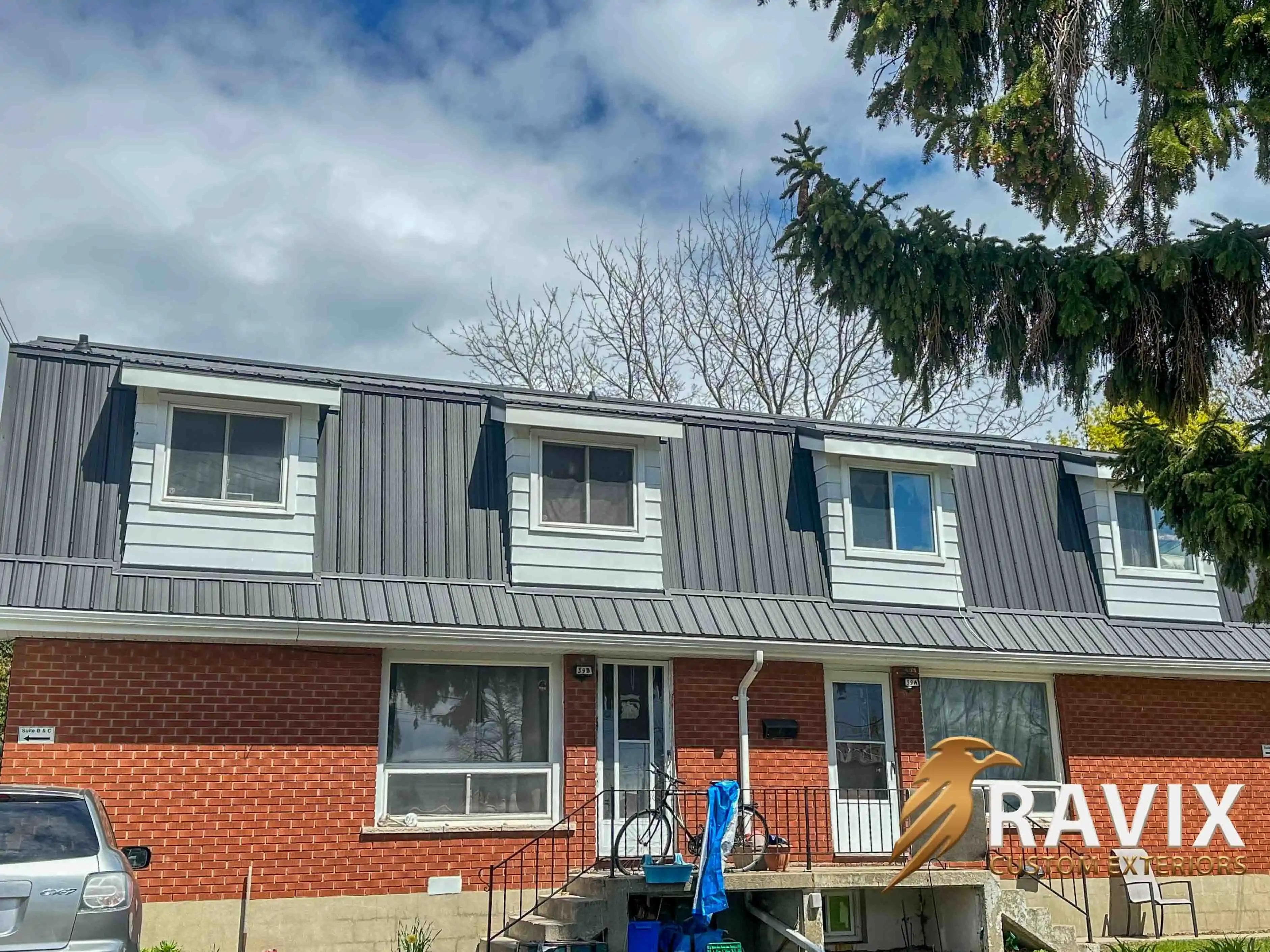 Front view of a brick multi-unit residential building with a new dark metal mansard-style roof and white window dormers.