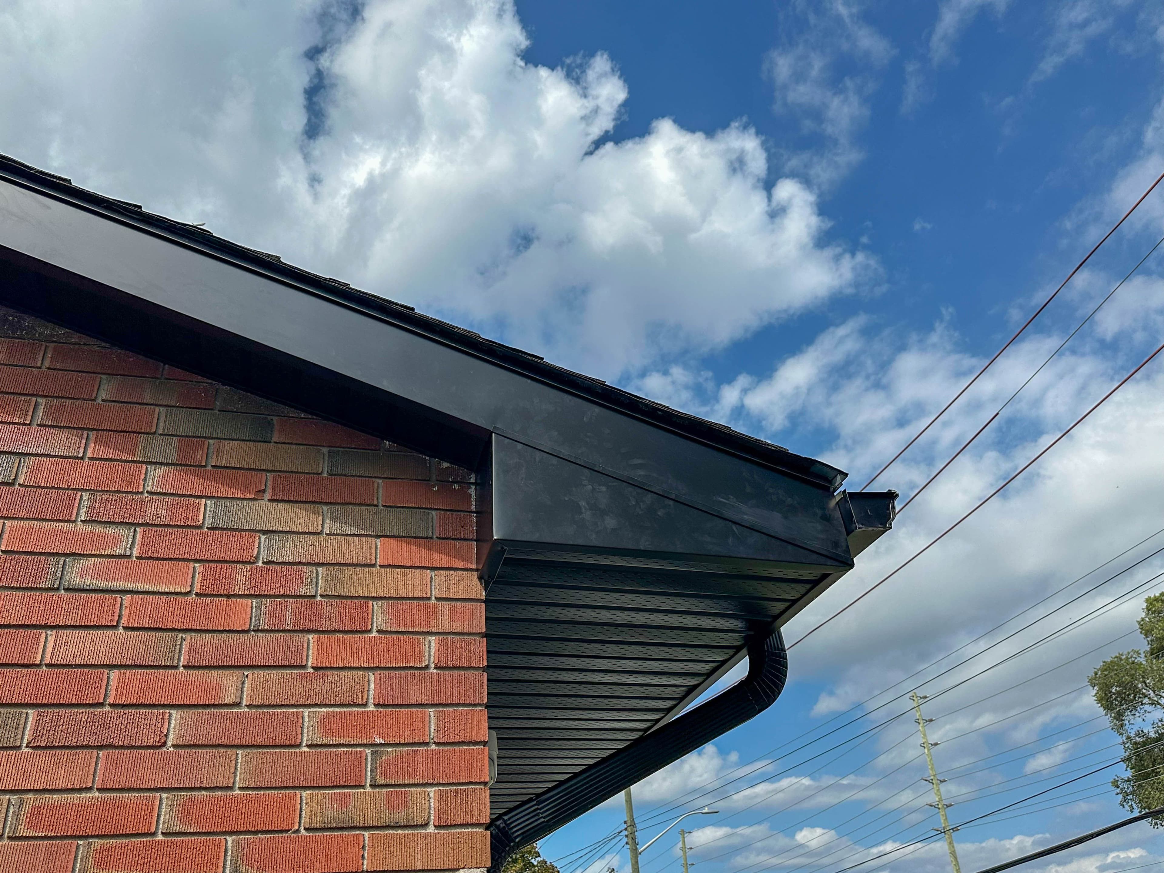 Close-up of new black soffit, fascia, and eavestrough installed on a red brick Belleville home