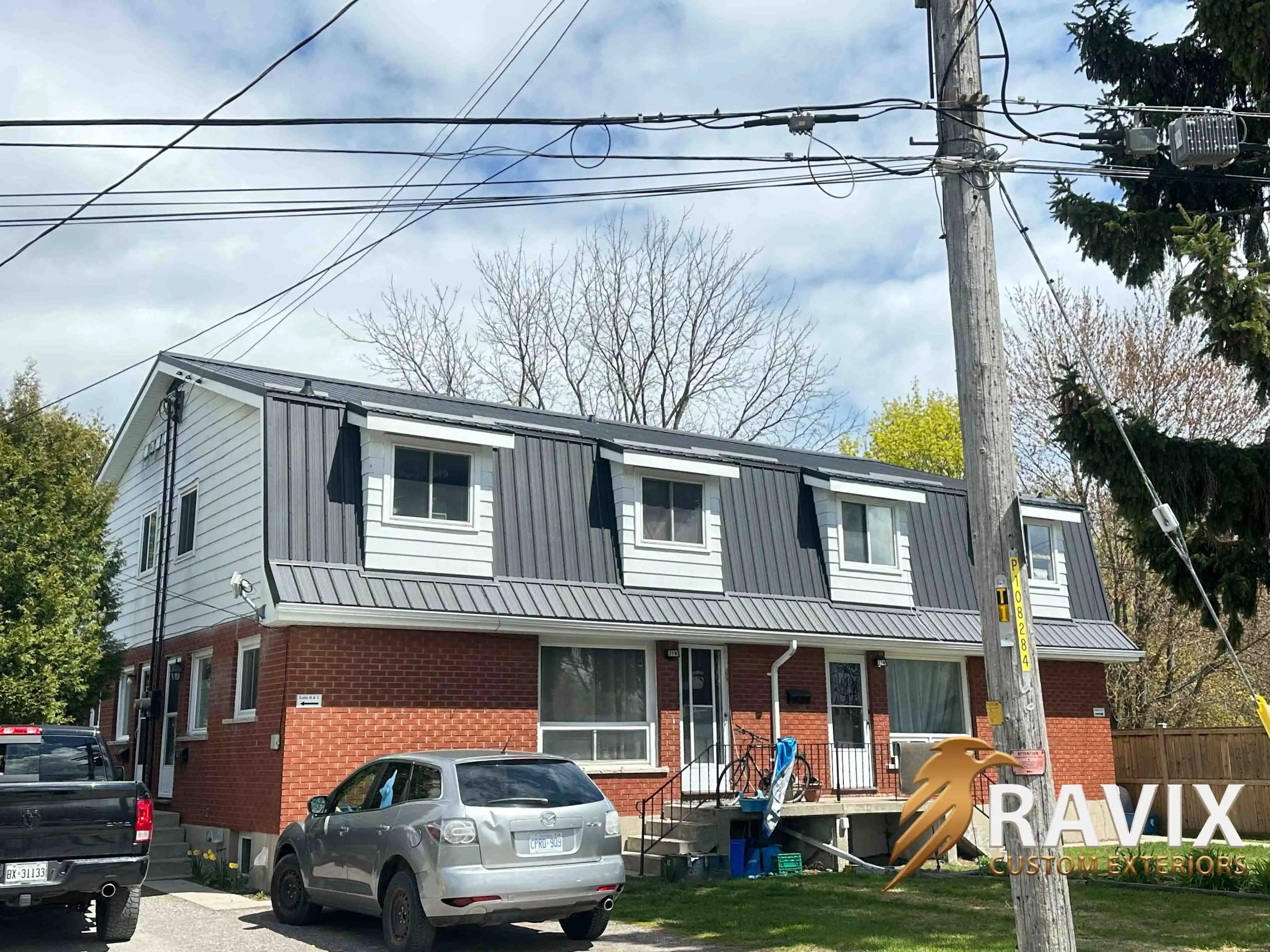 Multi-unit residential building with a dark metal roof, white dormers, brick exterior, and white eavestroughs.